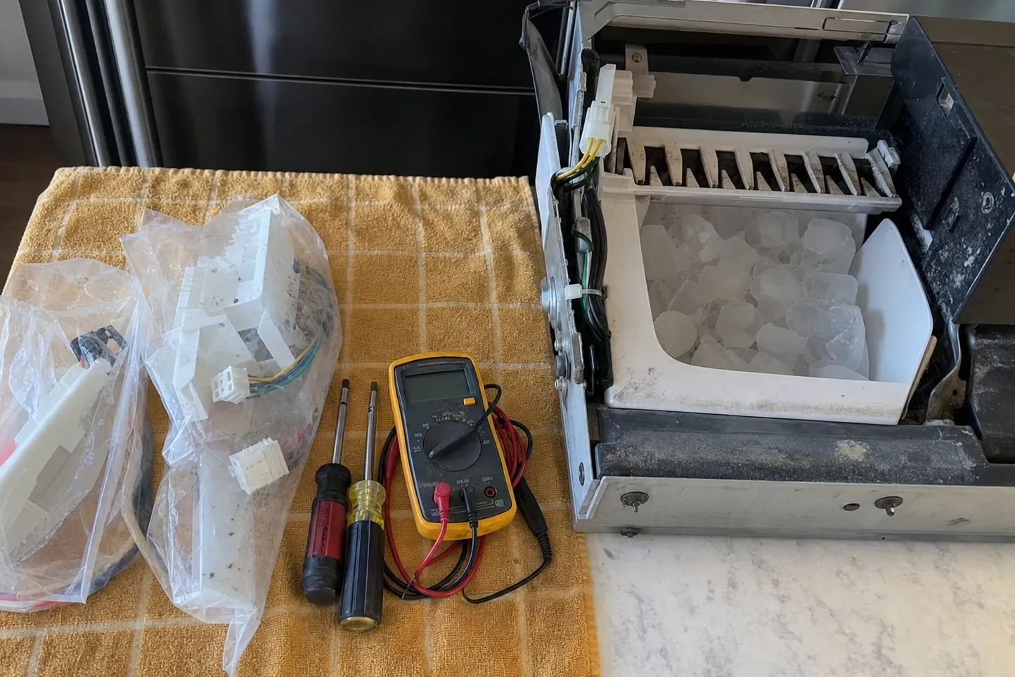 Ice maker module lifted out onto a counter, mould and bin still full of cubes, meter and bagged parts alongside